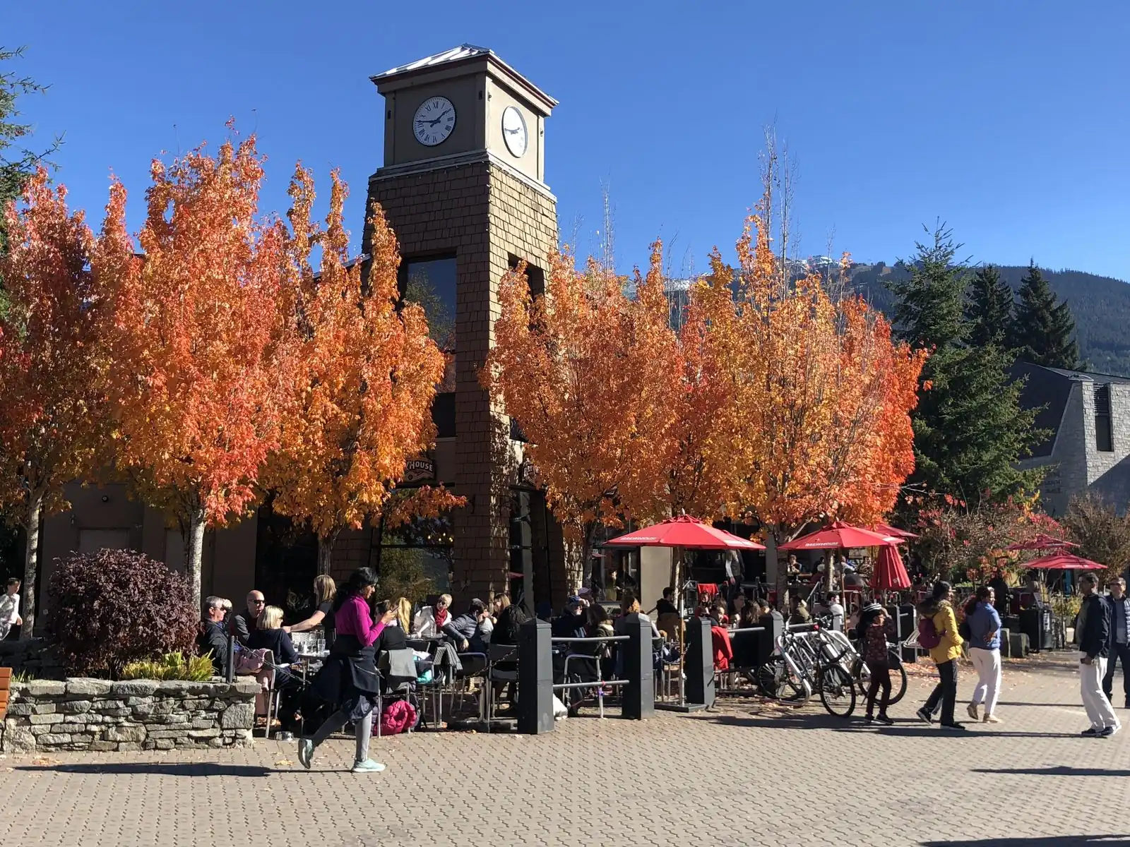 Torre del reloj en la Villa de Whistler, con hojas de otoño y mesas al aire libre