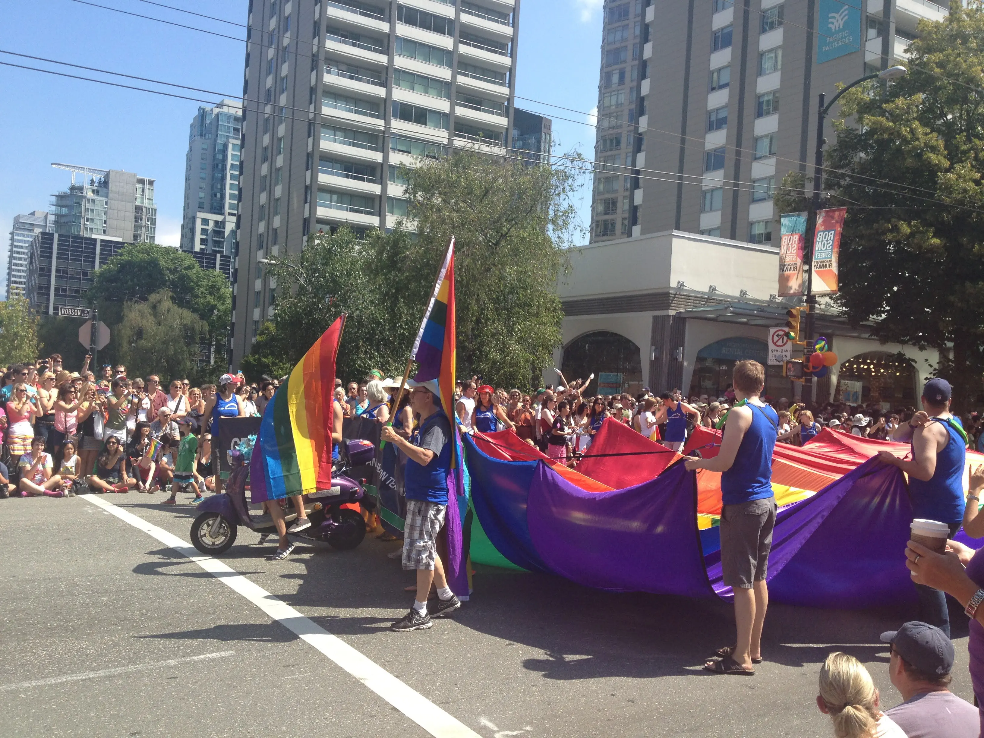 Multidão acompanhando a Pride Parade em Vancouver, com bandeiras nas cores do arco-íris